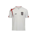 Camiseta de fútbol retro blanca de Inglaterra 2006 de Umbro con detalles de la Cruz de San Jorge en rojo y ribetes negros en las mangas. Escudo de Inglaterra con estrella dorada.