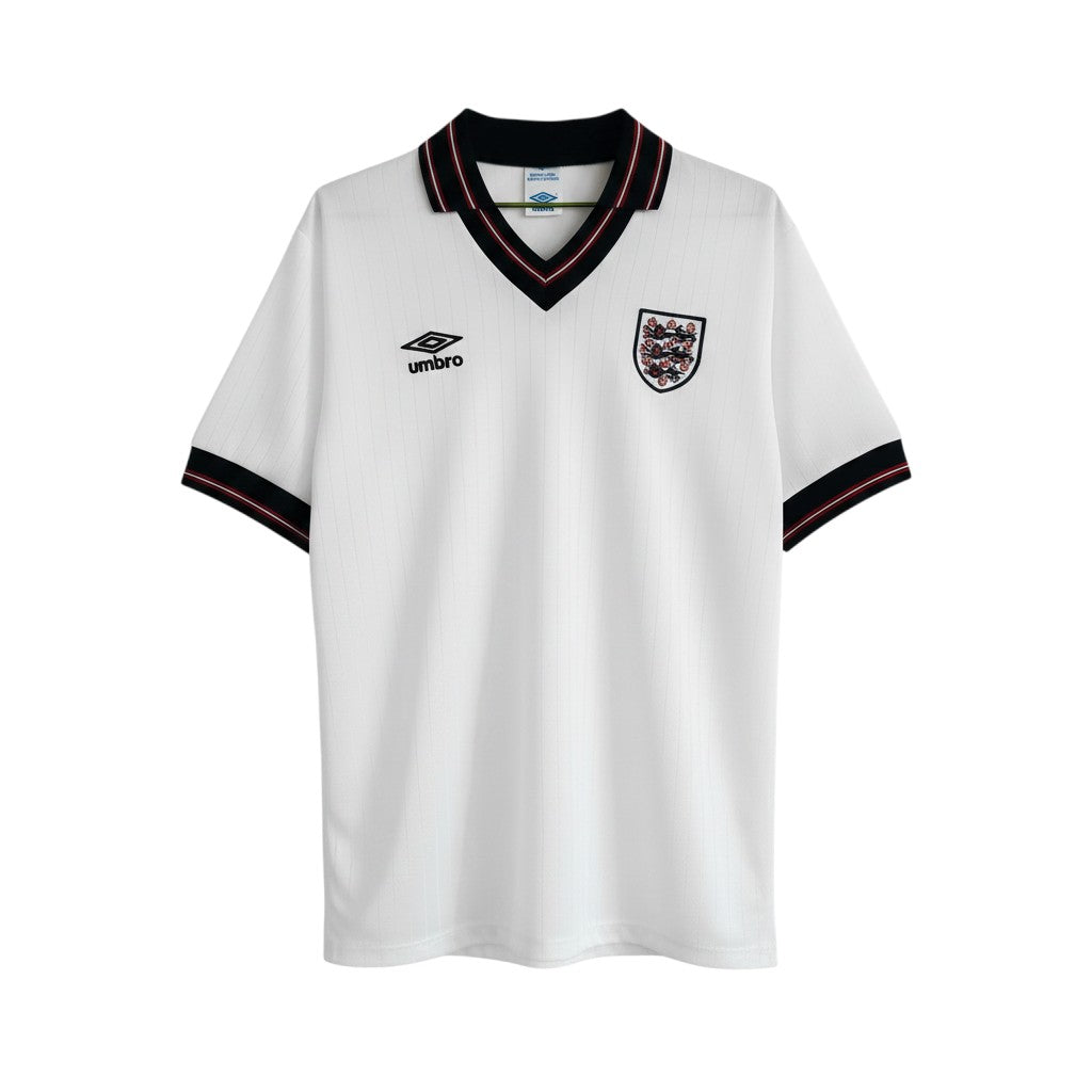 Camiseta de fútbol retro blanca de manga corta de Umbro para Inglaterra 1984, con cuello en V negro y ribete rojo, y escudo del equipo bordado.