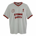 Hinchas Sportswear Store white Liverpool FC 1985/86 retro away shirt with red V-collar, sleeve cuffs, and 'Crown Paints' sponsor. Features LFC crest and commemorative patch.
